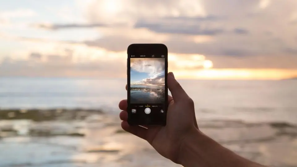 Gün batımında deniz manzarasının fotoğrafını çeken telefon