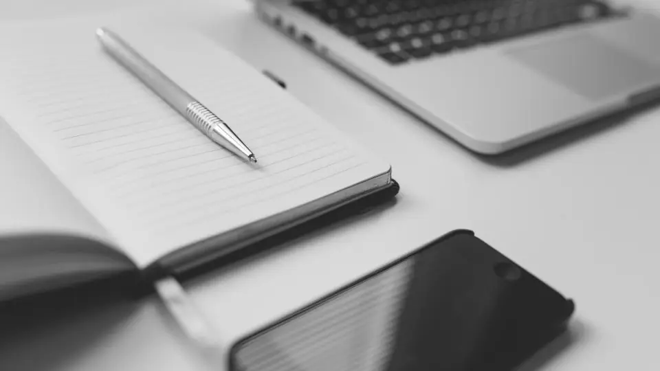 Masada açık defter, kalem, telefon ve dizüstü bilgisayar