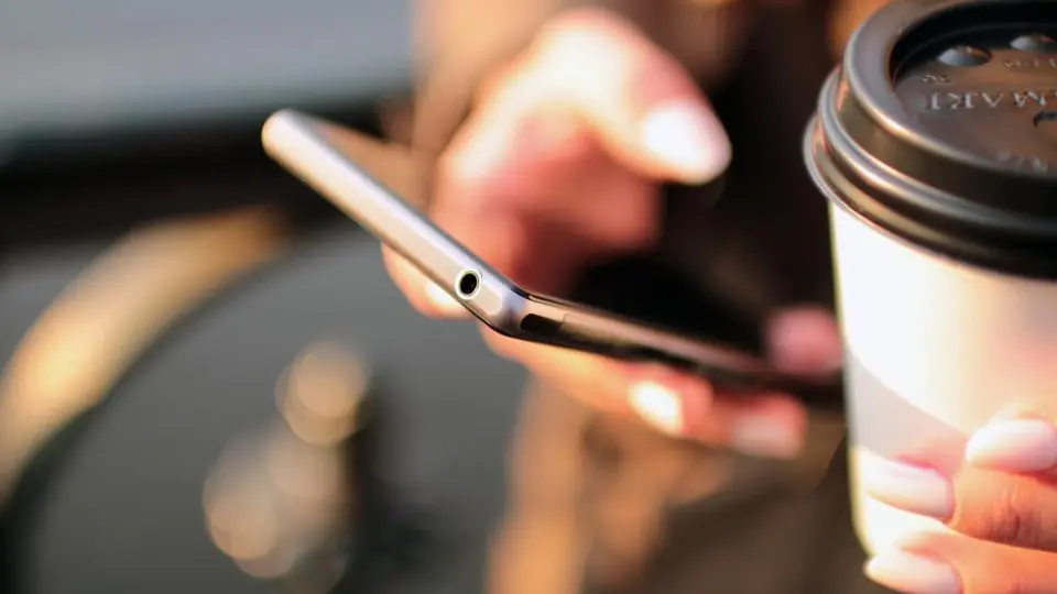 Kahve fincanının yanında akıllı telefon kullanan eller